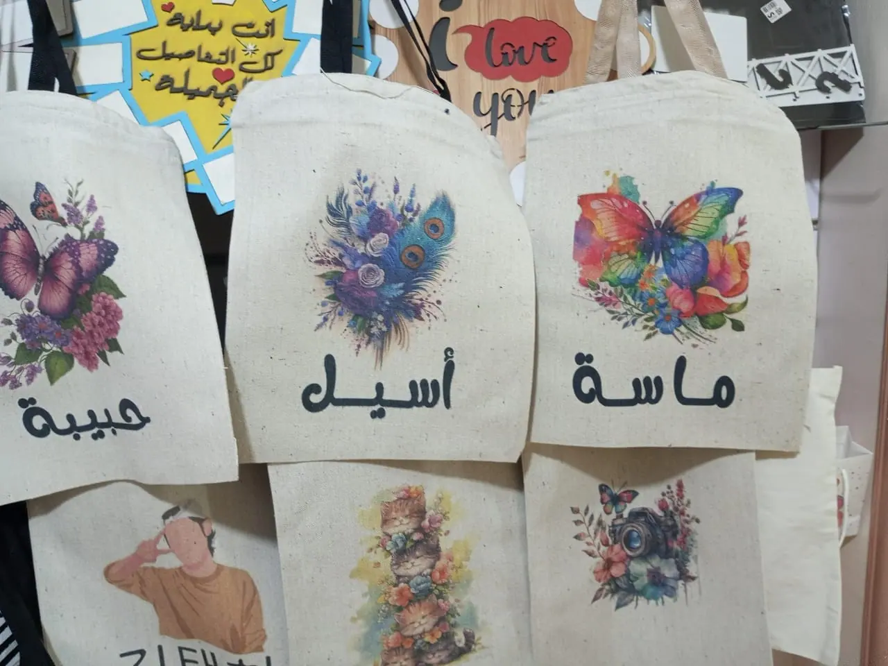 شنط قماش مطبوعة بأسماء بالعربي وتصاميم زهور معلقة للعرض